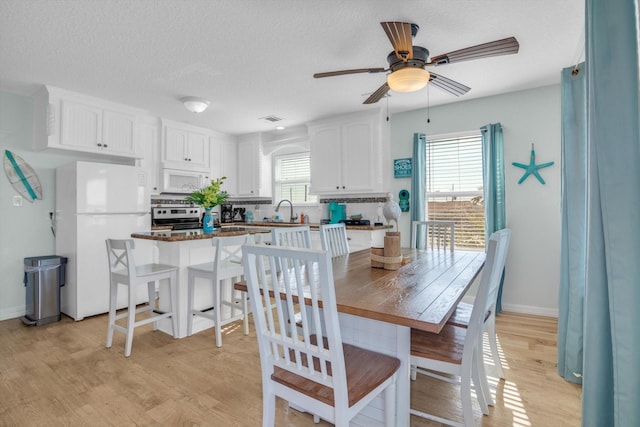 dining area with baseboards, light wood-style flooring, a textured ceiling, and ceiling fan