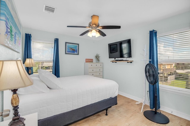 bedroom with a ceiling fan, wood finished floors, visible vents, and baseboards