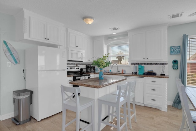 kitchen with white appliances, visible vents, a sink, white cabinetry, and dark countertops