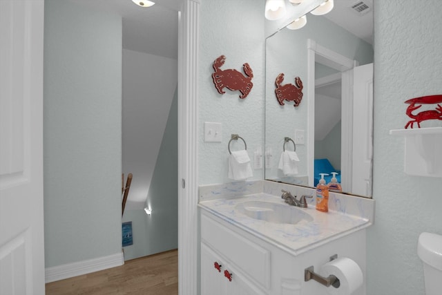 half bathroom featuring vanity, wood finished floors, visible vents, toilet, and a textured wall