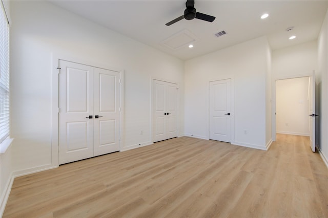 unfurnished bedroom with light wood-style flooring, a high ceiling, visible vents, multiple closets, and attic access