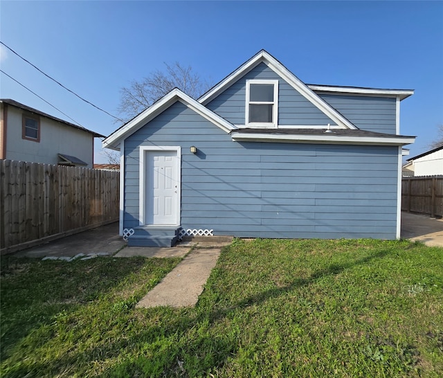 back of property featuring entry steps, fence, and a lawn