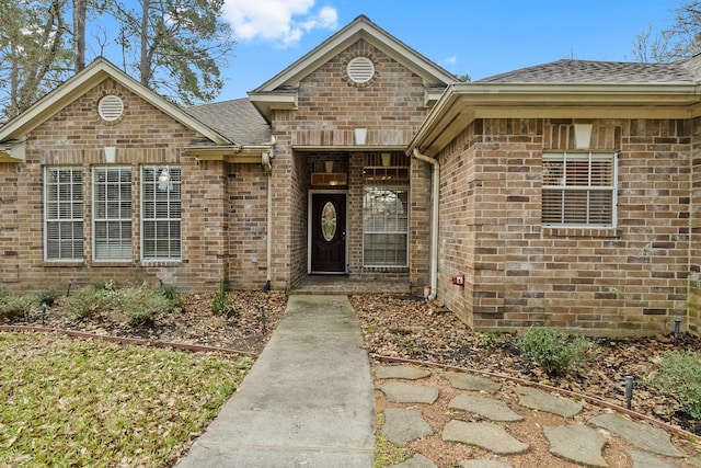 entrance to property with brick siding and a shingled roof