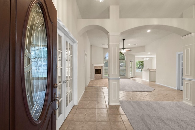 entrance foyer featuring ornate columns, arched walkways, a fireplace, light tile patterned floors, and vaulted ceiling