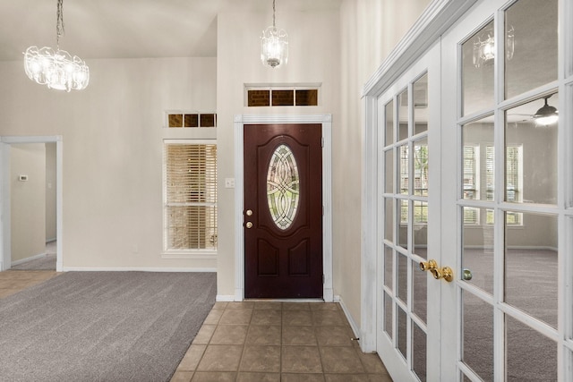 carpeted entrance foyer with tile patterned flooring, visible vents, baseboards, a high ceiling, and an inviting chandelier