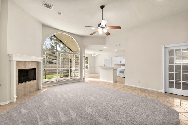 unfurnished living room featuring visible vents, light carpet, a ceiling fan, light tile patterned floors, and a tile fireplace