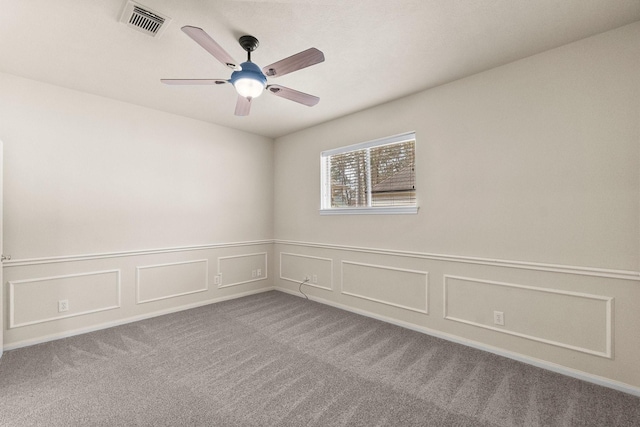 spare room featuring a decorative wall, carpet, visible vents, and ceiling fan