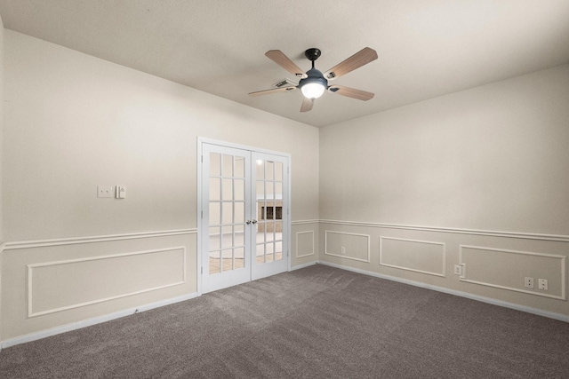 spare room featuring dark carpet, wainscoting, french doors, a decorative wall, and a ceiling fan