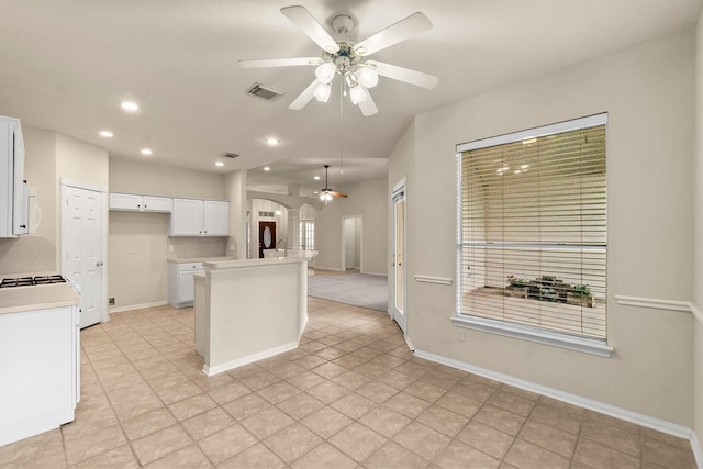 kitchen with visible vents, an island with sink, gas stove, white cabinets, and light countertops