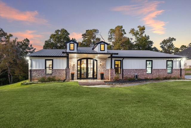 view of front of home featuring a lawn, metal roof, french doors, board and batten siding, and brick siding