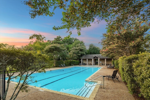 pool at dusk featuring an outbuilding, a patio, a community pool, fence, and an exterior structure