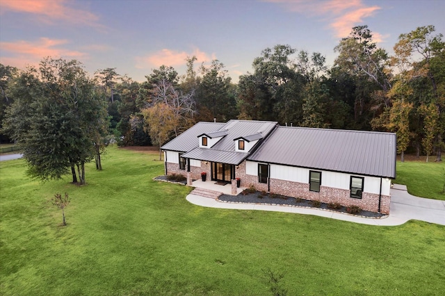 view of front of house featuring a yard, covered porch, metal roof, stone siding, and driveway