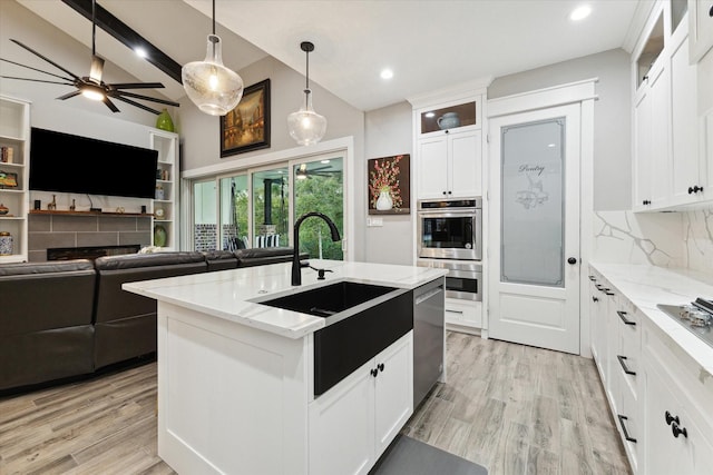 kitchen featuring light stone counters, a sink, open floor plan, appliances with stainless steel finishes, and tasteful backsplash