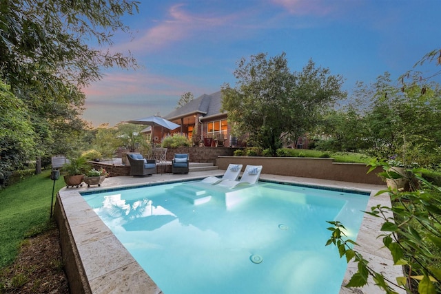 pool at dusk with a patio area, outdoor lounge area, and a lawn