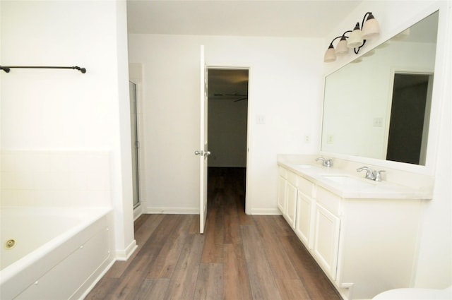 bathroom with baseboards, wood finished floors, a garden tub, and a sink