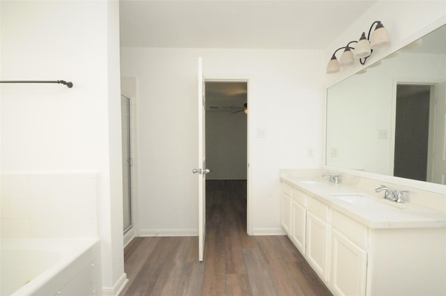 bathroom with a garden tub, a sink, wood finished floors, double vanity, and baseboards