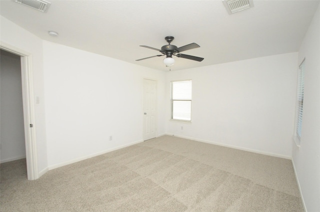 unfurnished room with a ceiling fan, light colored carpet, visible vents, and baseboards