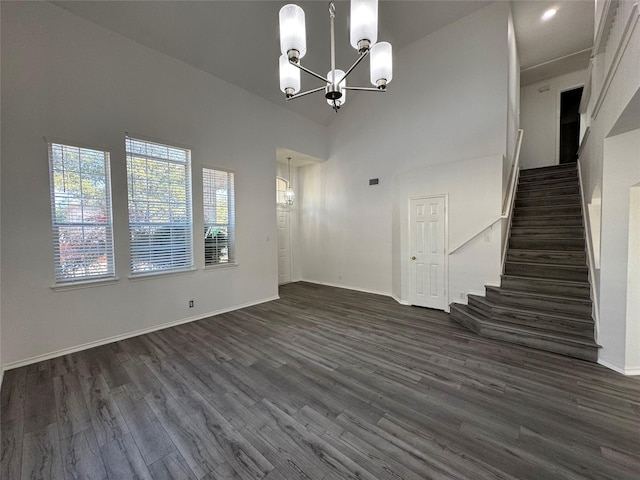 interior space with dark wood-style floors, a notable chandelier, a towering ceiling, baseboards, and stairs