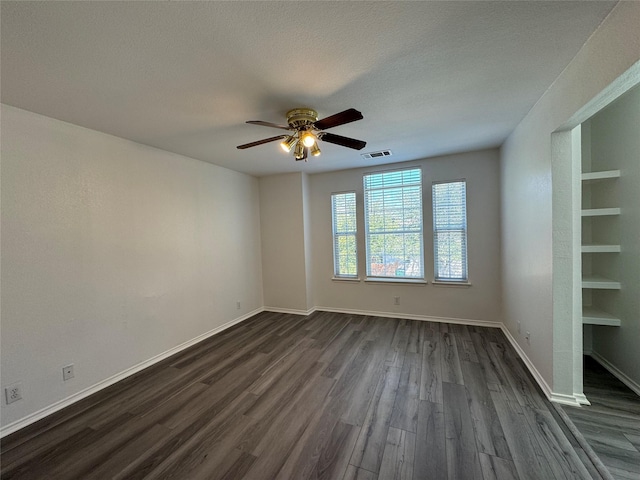 empty room featuring baseboards, visible vents, a ceiling fan, dark wood-style flooring, and a textured ceiling