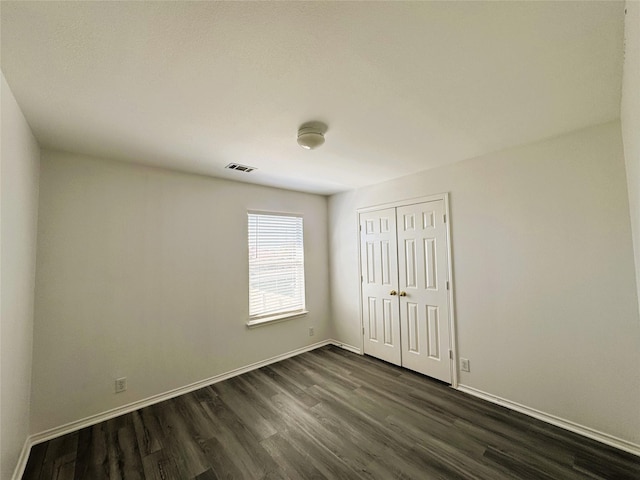 unfurnished room with dark wood-style flooring, visible vents, and baseboards