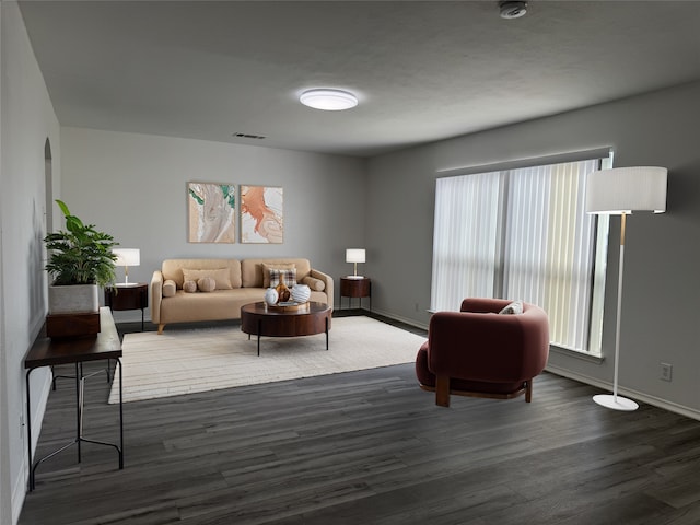 living area featuring arched walkways, dark wood finished floors, visible vents, and baseboards