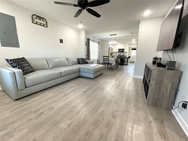 living room featuring baseboards, electric panel, ceiling fan, and light wood finished floors