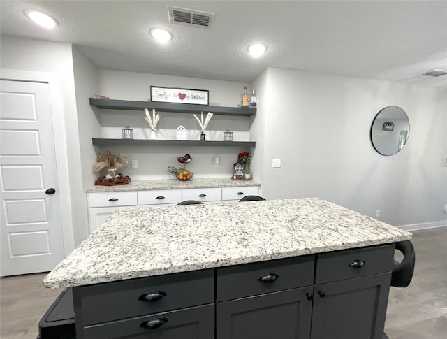 kitchen featuring light stone countertops, visible vents, open shelves, and a center island