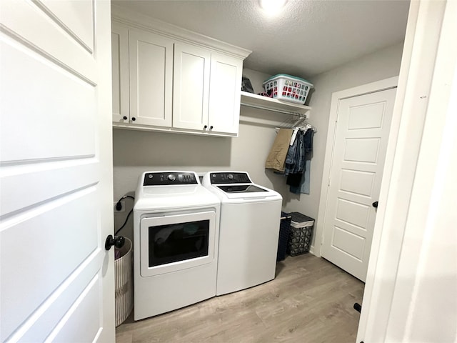 clothes washing area featuring a textured ceiling, washer and clothes dryer, cabinet space, and light wood-style floors