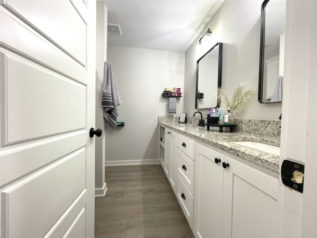 full bath featuring double vanity, baseboards, visible vents, wood finished floors, and a sink