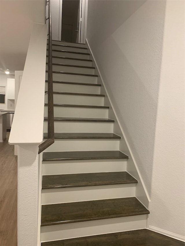 stairs with baseboards, wood finished floors, and a textured wall