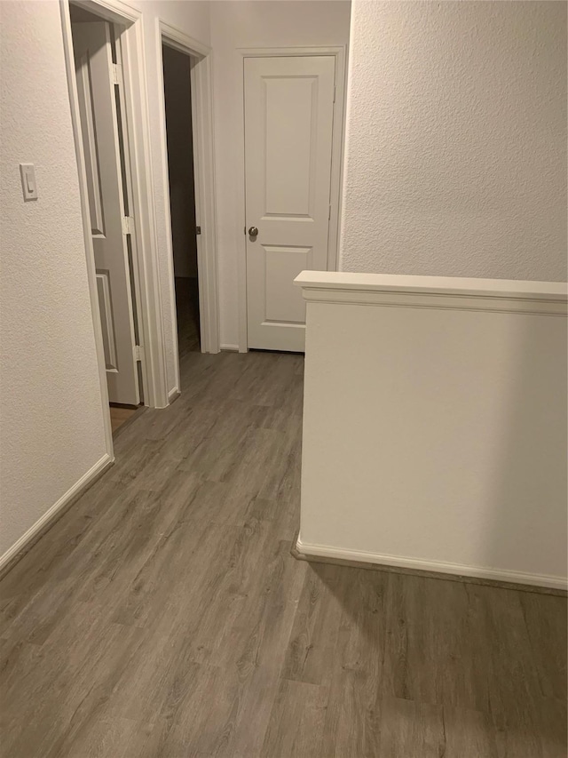 hallway with a textured wall, wood finished floors, and baseboards