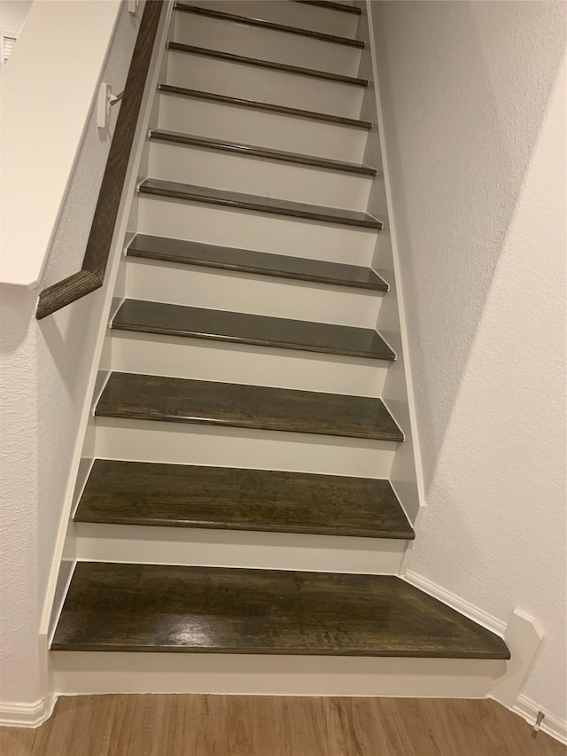 staircase featuring wood finished floors and a textured wall