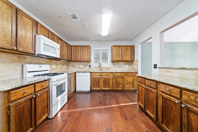 kitchen with white appliances, brown cabinetry, visible vents, dark wood finished floors, and a sink