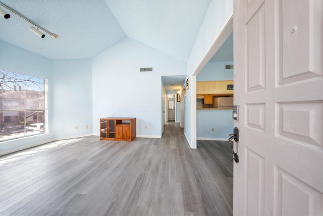 unfurnished living room featuring vaulted ceiling, wood finished floors, visible vents, and baseboards