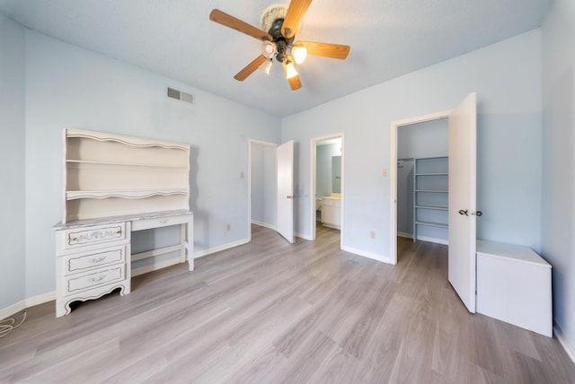 unfurnished bedroom featuring baseboards, wood finished floors, visible vents, and a walk in closet