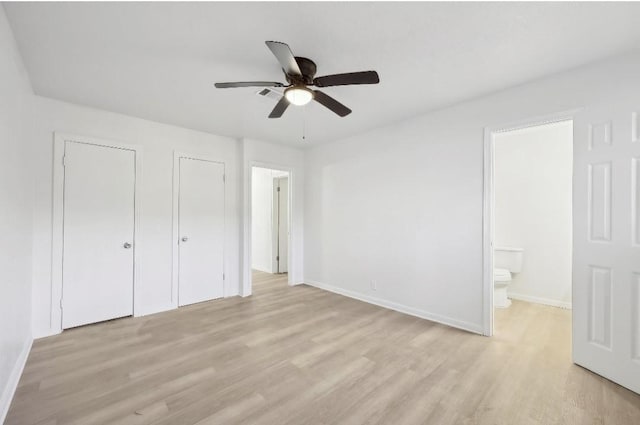 unfurnished bedroom with two closets, light wood-style flooring, ensuite bathroom, a ceiling fan, and baseboards