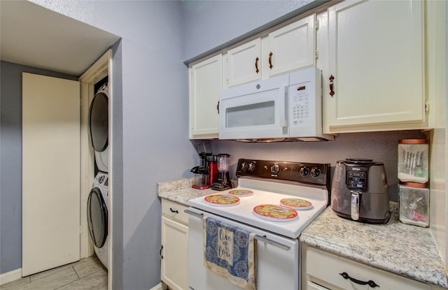 kitchen featuring white cabinets, stacked washing maching and dryer, light stone countertops, white appliances, and baseboards