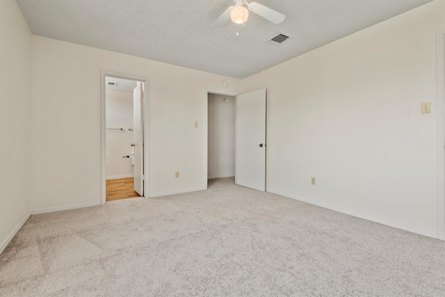 unfurnished bedroom featuring baseboards, visible vents, a ceiling fan, ensuite bath, and carpet flooring