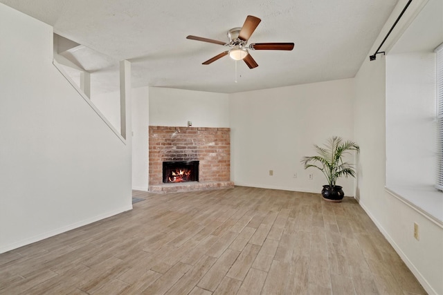 unfurnished living room with light wood-type flooring, a fireplace, a ceiling fan, and baseboards