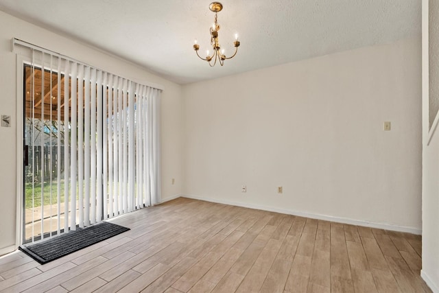 spare room featuring light wood finished floors, plenty of natural light, baseboards, and a notable chandelier