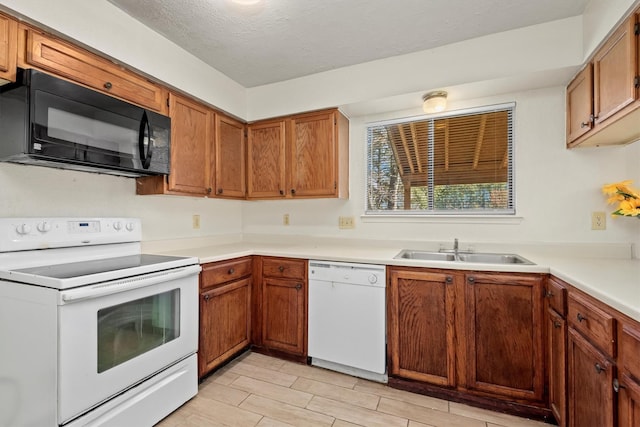 kitchen featuring white appliances, brown cabinetry, light countertops, a textured ceiling, and a sink