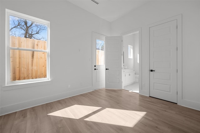 unfurnished bedroom with baseboards, ensuite bath, and wood finished floors