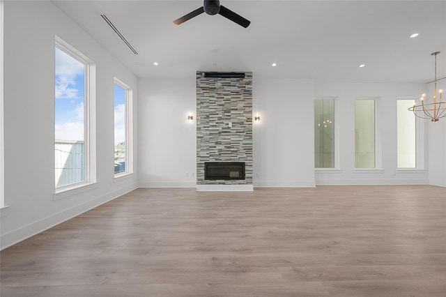 unfurnished living room with ceiling fan with notable chandelier, light wood finished floors, a tiled fireplace, and recessed lighting