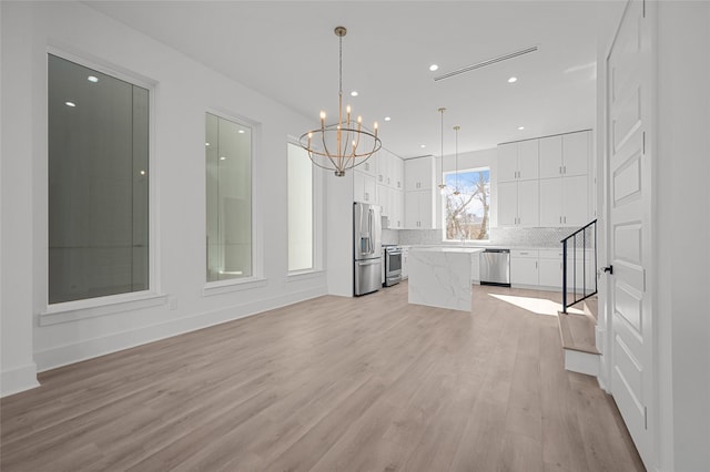 interior space featuring appliances with stainless steel finishes, a center island, light wood-type flooring, and white cabinets