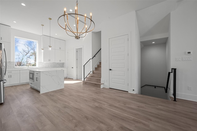 kitchen with a center island, stainless steel appliances, light wood-style floors, white cabinetry, and backsplash