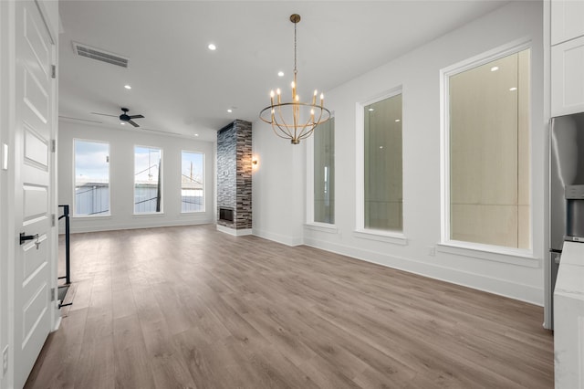 unfurnished dining area featuring visible vents, wood finished floors, ceiling fan with notable chandelier, a stone fireplace, and recessed lighting