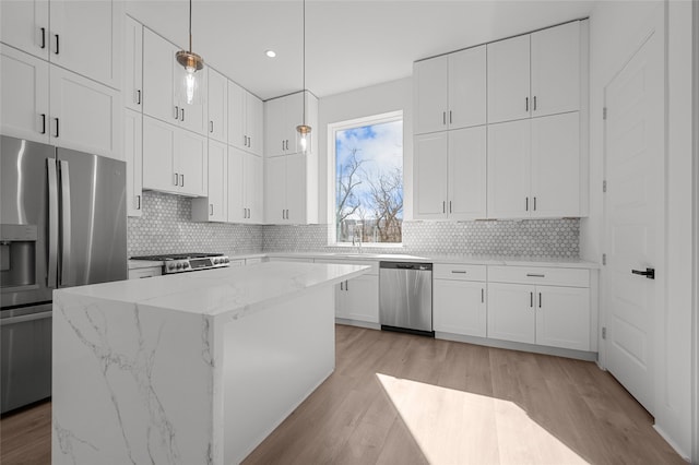 kitchen with light wood finished floors, tasteful backsplash, appliances with stainless steel finishes, white cabinets, and a kitchen island