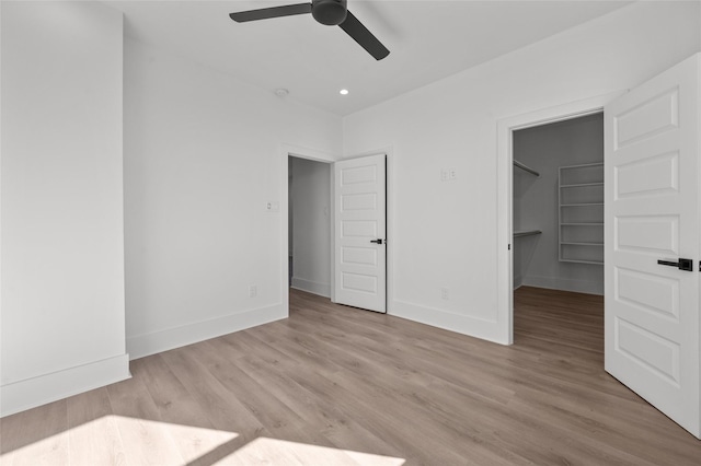 unfurnished bedroom with ceiling fan, a walk in closet, light wood-style flooring, and baseboards