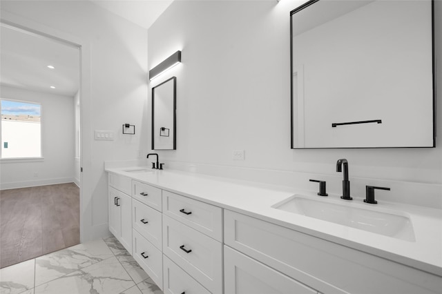 bathroom featuring double vanity, marble finish floor, baseboards, and a sink