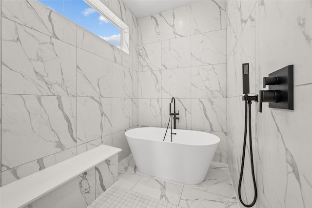 full bathroom with marble finish floor, a freestanding bath, and stone wall